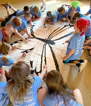 Students sit and gather around large butterfly they are drawing.