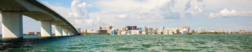 skyline of a city as you look over blue and green water with a bridge by the side