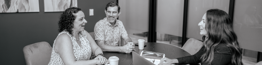 black and white image of three people sitting around a table smiling and talking to each other