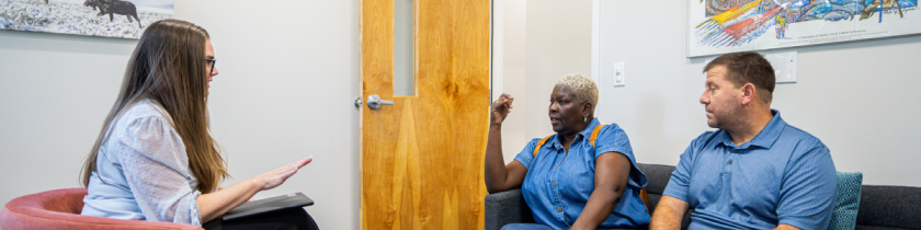 three people sitting on chairs and couches in an office with the door open talking to each other