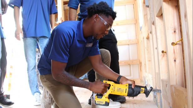 Young man kneels on one knee using tool to build tiny house.