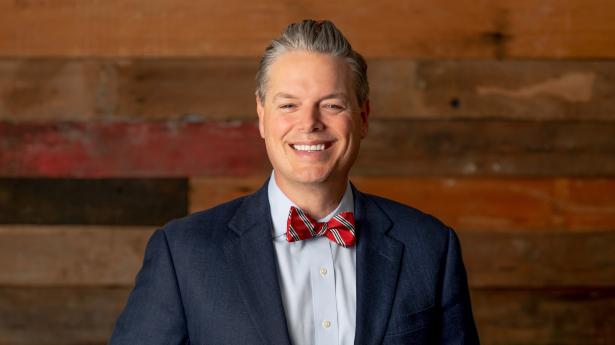 Gulf Coast's new President | CEO Phillip Lanham smiles at camera with dark wood wall in background.