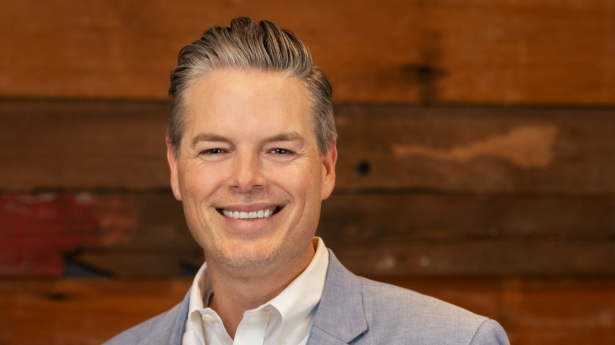 Phillip Lanham, Gulf Coast's President | CEO, smiles at camera with dark wood wall in background and grey suit jacket with white shirt underneath.