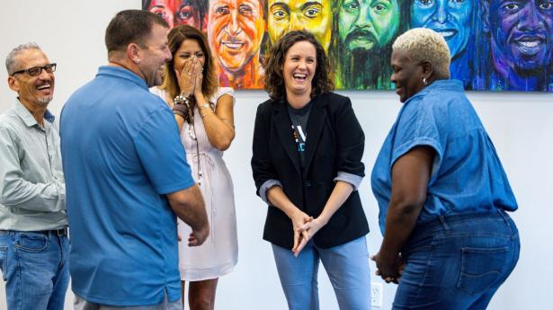 five people standing in front of colorful paintings laughing together