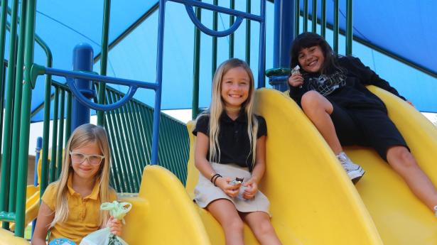 3 children on yellow slides smiling at the camera