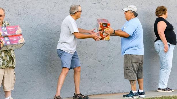 Four people stand outside; two people pass a box to each other.