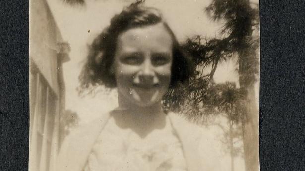 A photo of a woman in the 1936 with short dark hair and palm trees in background.