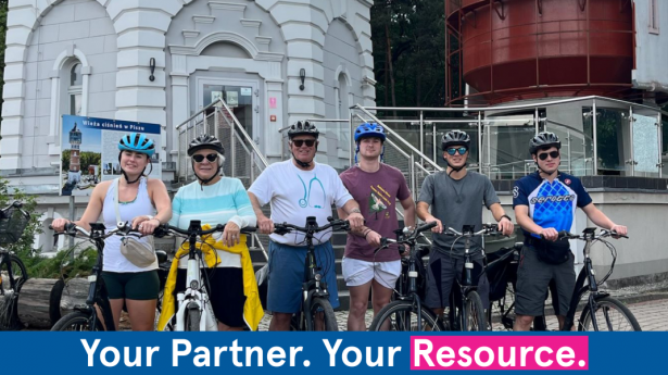 six people on bikes outside a big tower smiling at the camera