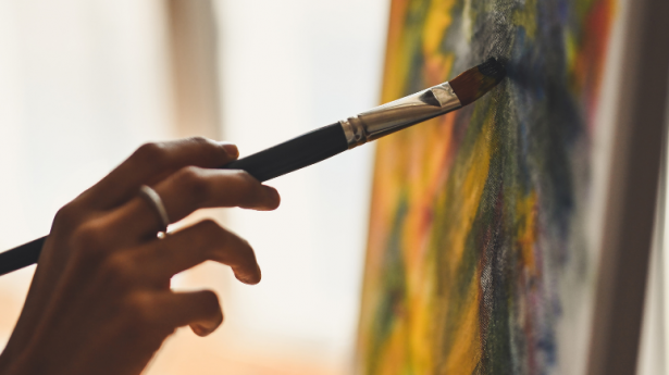 hand holding a black paint brush against a piece of artwork