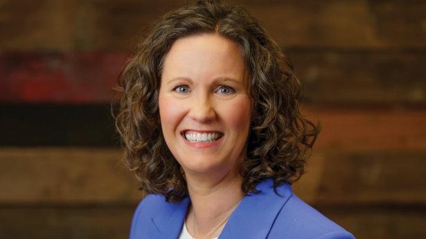 woman in a bright blue jacket and white shirt smiles at the camera against a dark wood wall