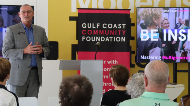 man standing in front of a room of people with a sign next to him that says Gulf Coast Community Foundation