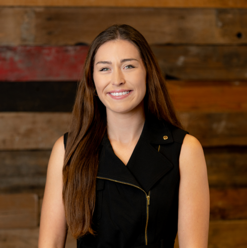 woman wearing black dress smiling against a wood wall