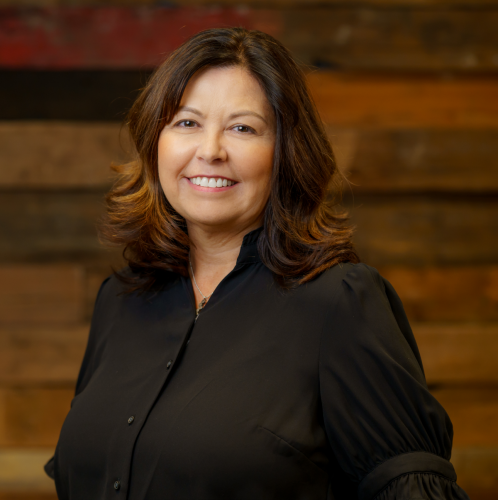 women in a black shirt smiling at the camera against a wooden wall