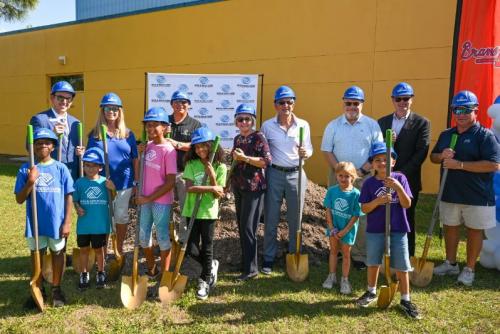 Eight adults and six children stand smiling with shovels in hand and helmets on their heads.