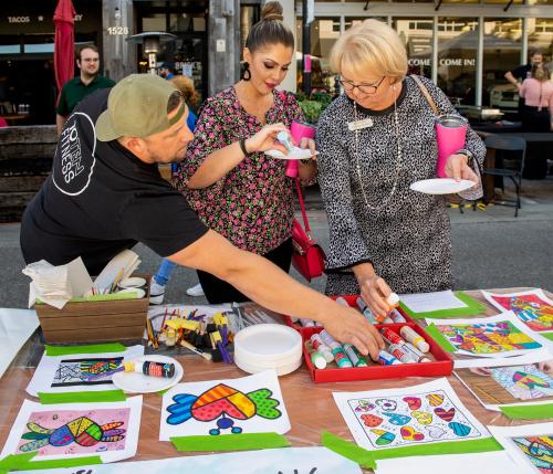 Three people decorate hearts with paint markers and paper plates in hand.