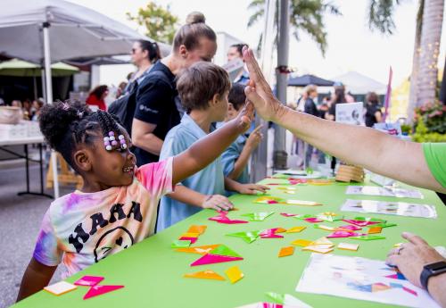 At an outdoor block party, Better Together, a young girl high fives one of the booth attendees.