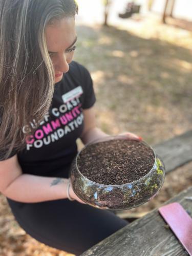 Woman wearing Gulf Coast Community Foundation shirt holds composted soil.