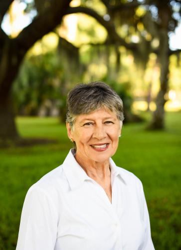 One woman with dark, grey hair and white blouse stands outside smiling.