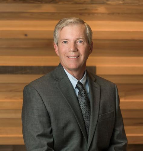 David Sessions stands, smiling in grey suit with Gulf Coast Community Foundation's wood wall in background.