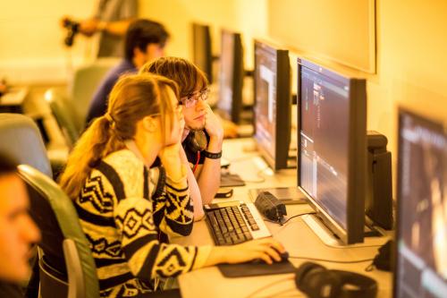 Two students sit side by side looking at computer screen.