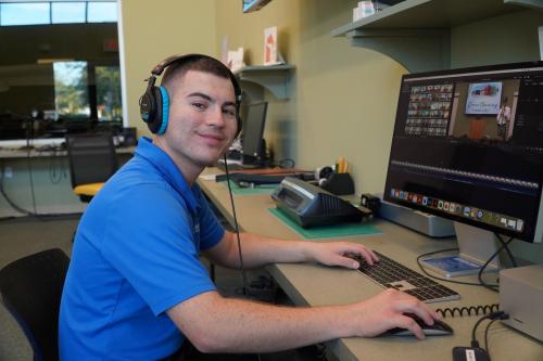 One young man with headphones on, smiles at camera.