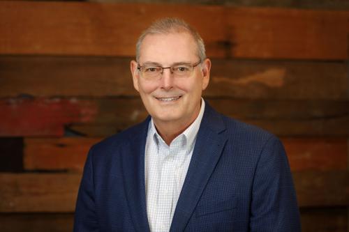 One man with glasses smiles with blue suit jacket and shirt.