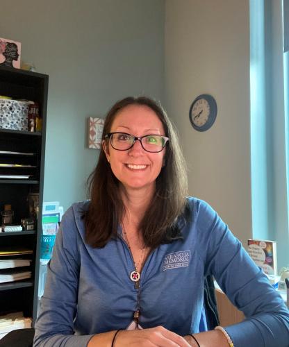 One woman with glasses and medium length hair and blue shirt smiles at camera.