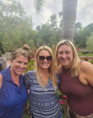 Three women, standing together, smiling outdoors.