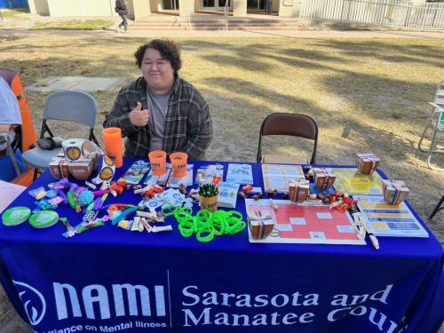 One woman sits behind table at NAMI Walks mental health care event.