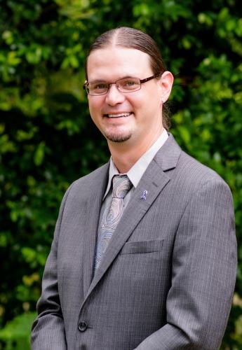 One man with glasses and a suit smiling at camera.