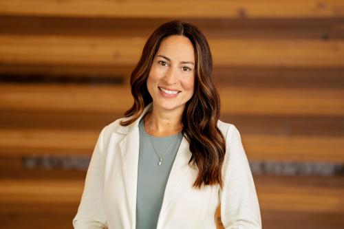 One woman smiles at camera with long brown hair, white jacket, and light blue shirt. 