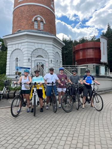 Six people stand outside with bicycles and helmets on. Two circular building structures stand tall in the background.