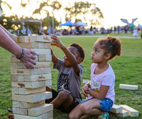 Two children sitting outside in the grass at The Bay Park playing a large size game of The Bay jenga.