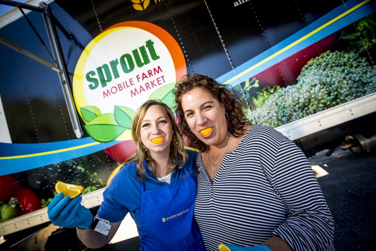 Two women standing in front of a truck with a sprout sign.